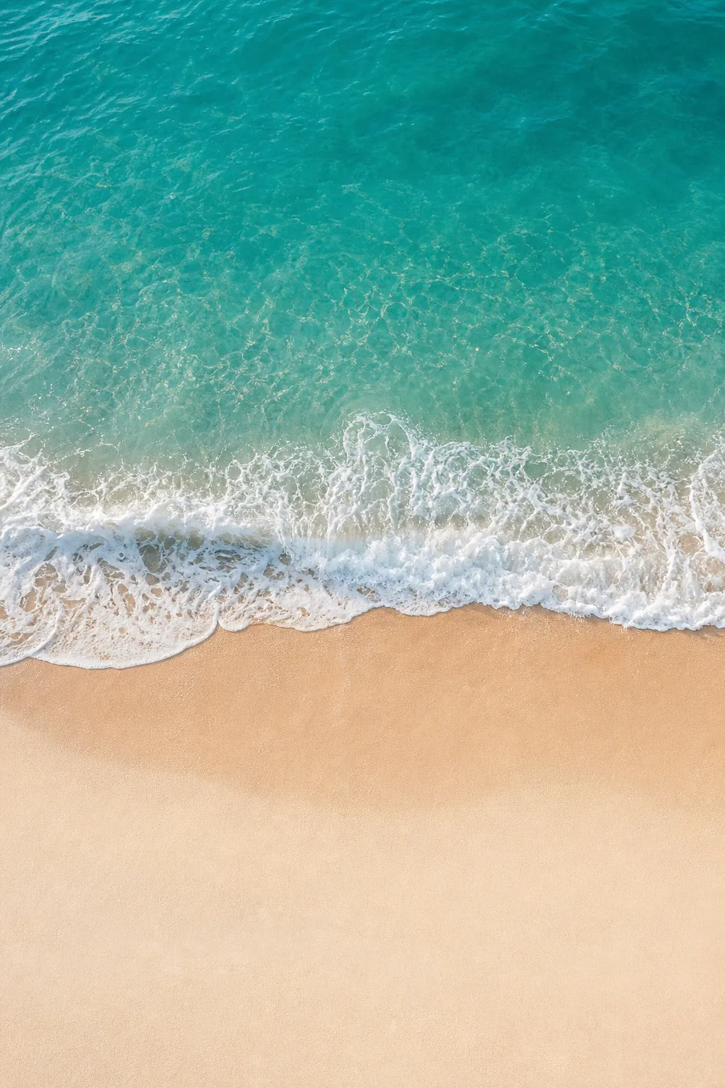 Aerial view of a teal wave curling onto pale sand